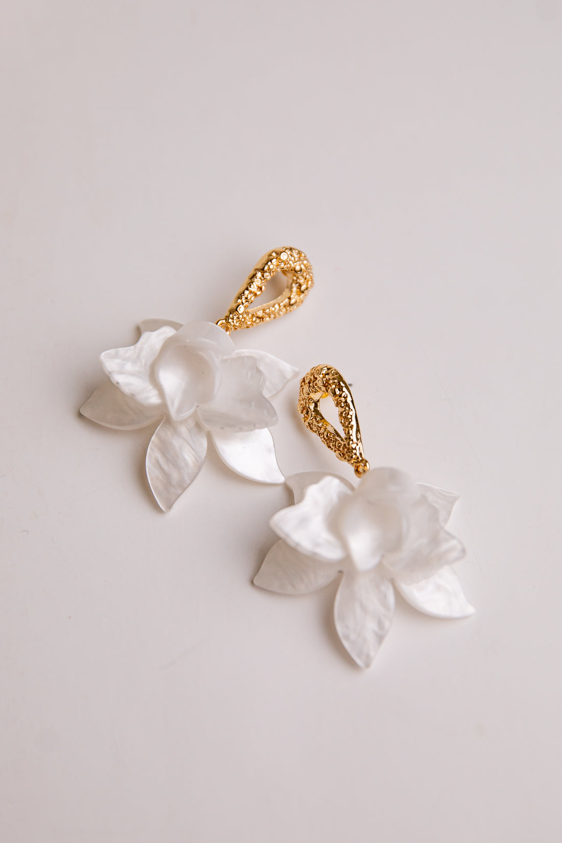 Gold and white floral earrings on a light background