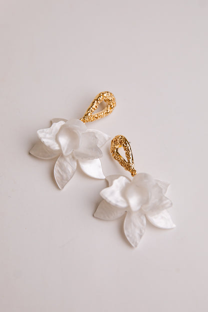 Gold and white floral earrings on a light background