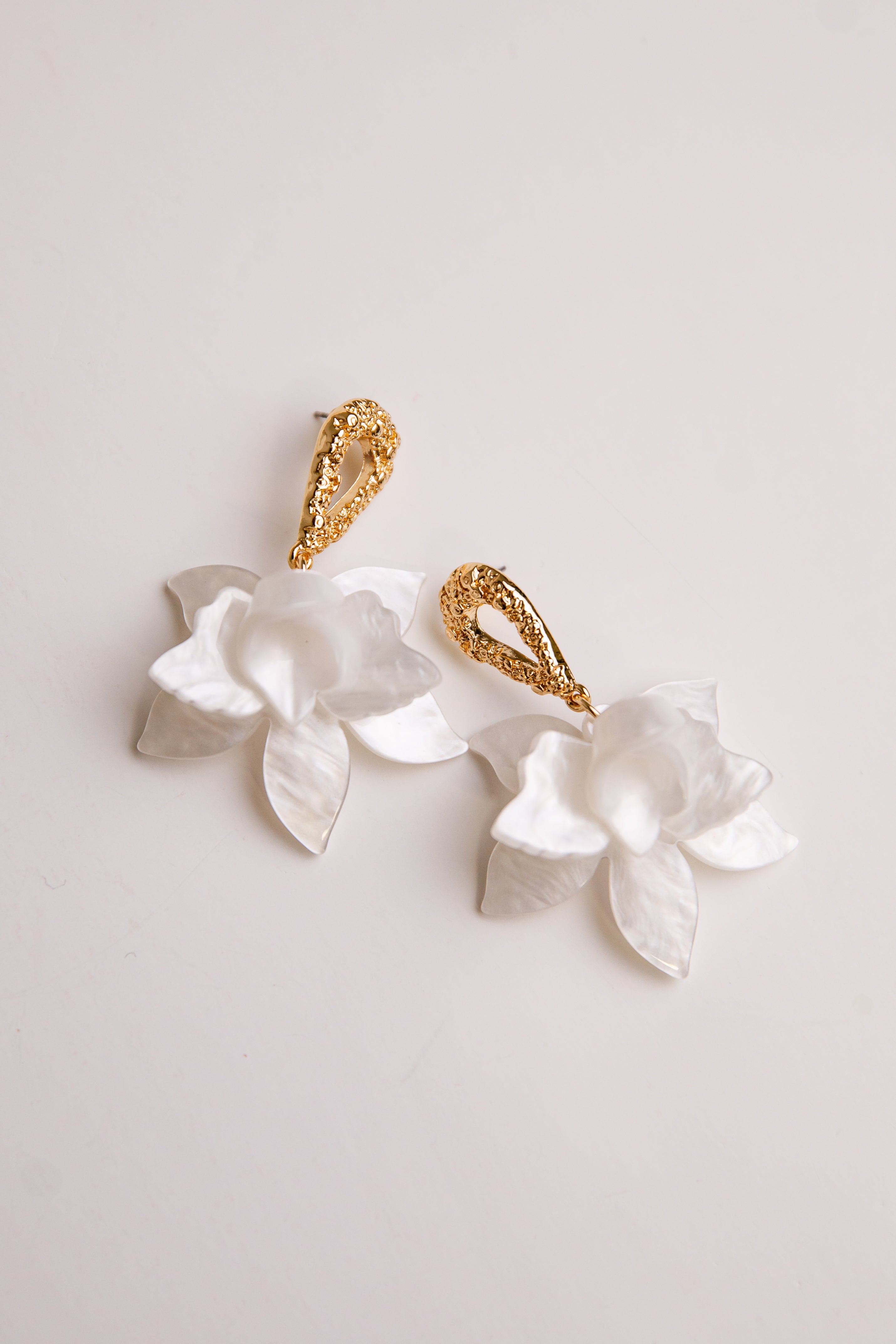 Pair of earrings with white floral designs and gold accents on a light gray background