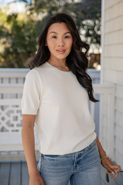 Woman wearing a white t-shirt and blue jeans standing on a porch.