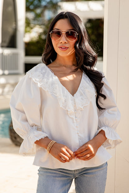 Woman wearing a white blouse and sunglasses by a poolside.