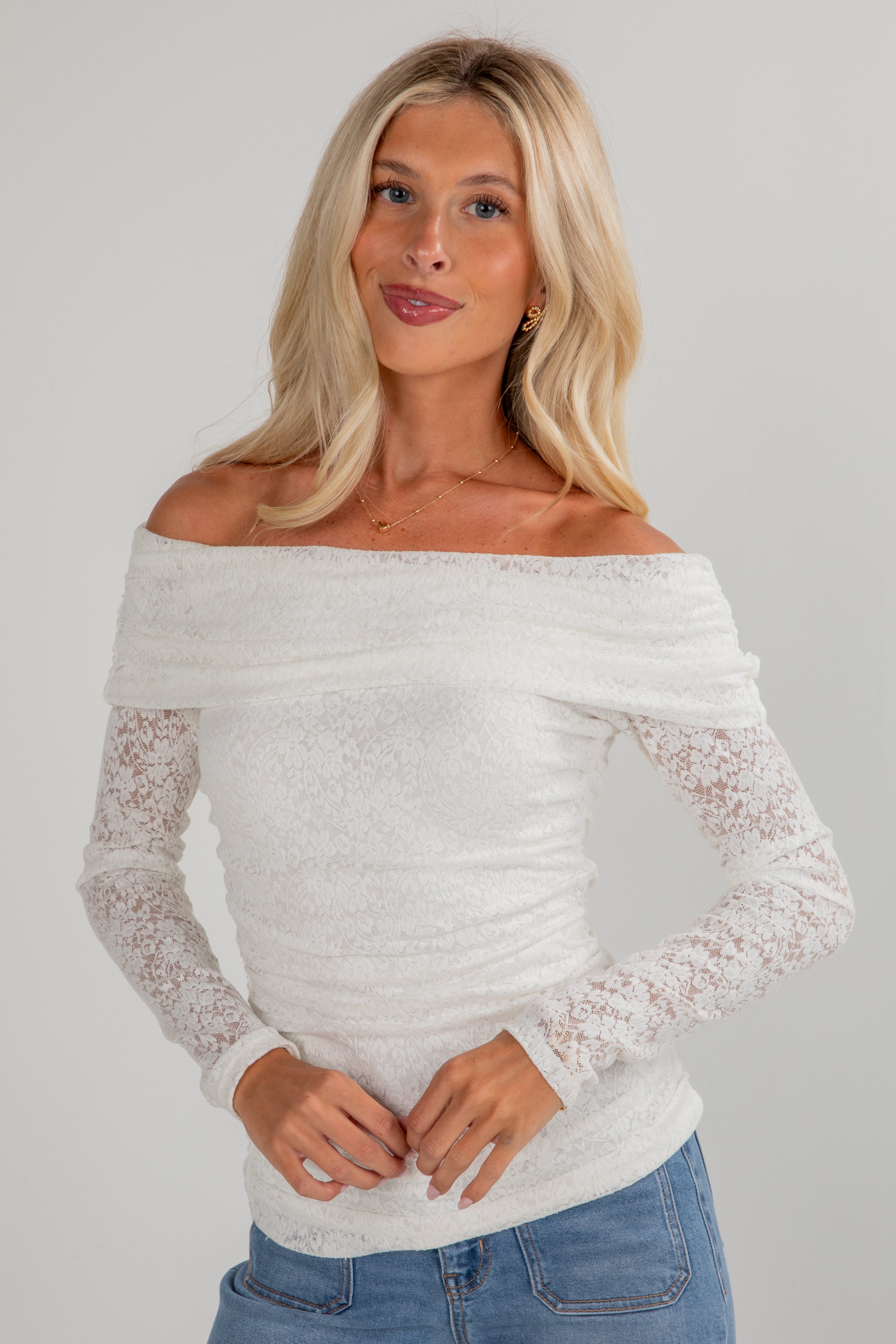 Woman wearing a white off-shoulder top with lace sleeves against a plain background