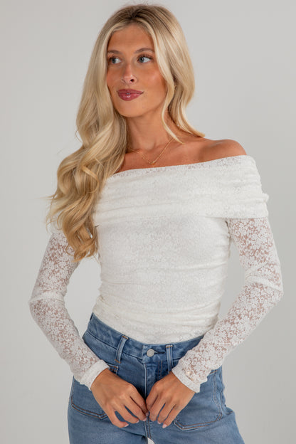 Woman wearing a white off-shoulder top with lace sleeves against a gray background