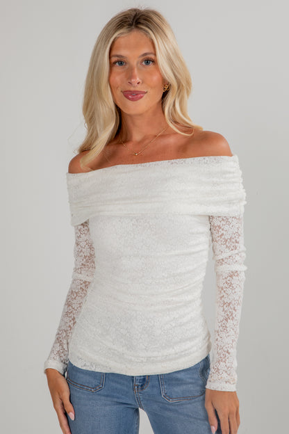 Woman wearing a white off-shoulder top with lace sleeves against a gray background