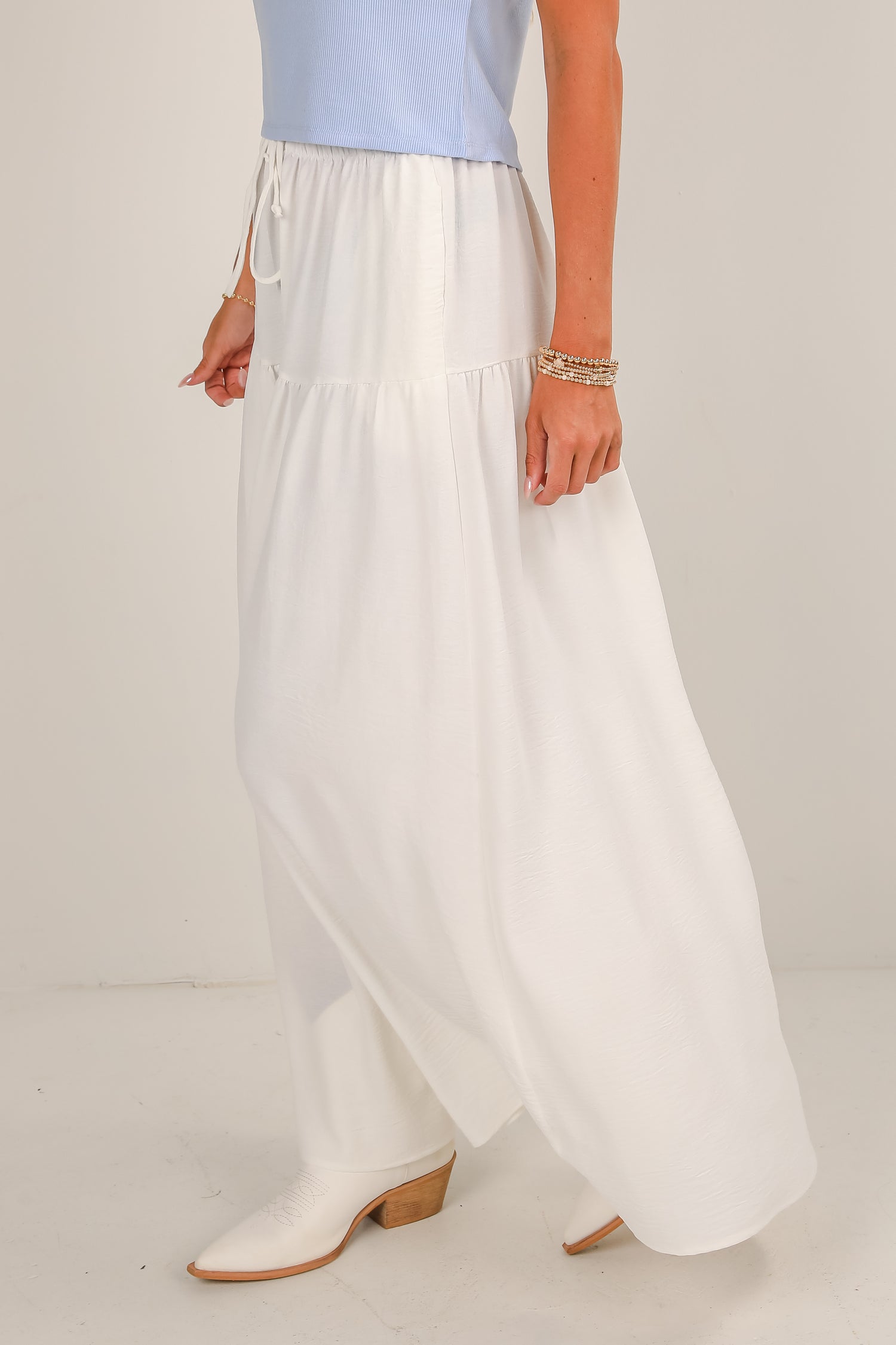 Person wearing a light blue top and white wide-leg pants on a plain background