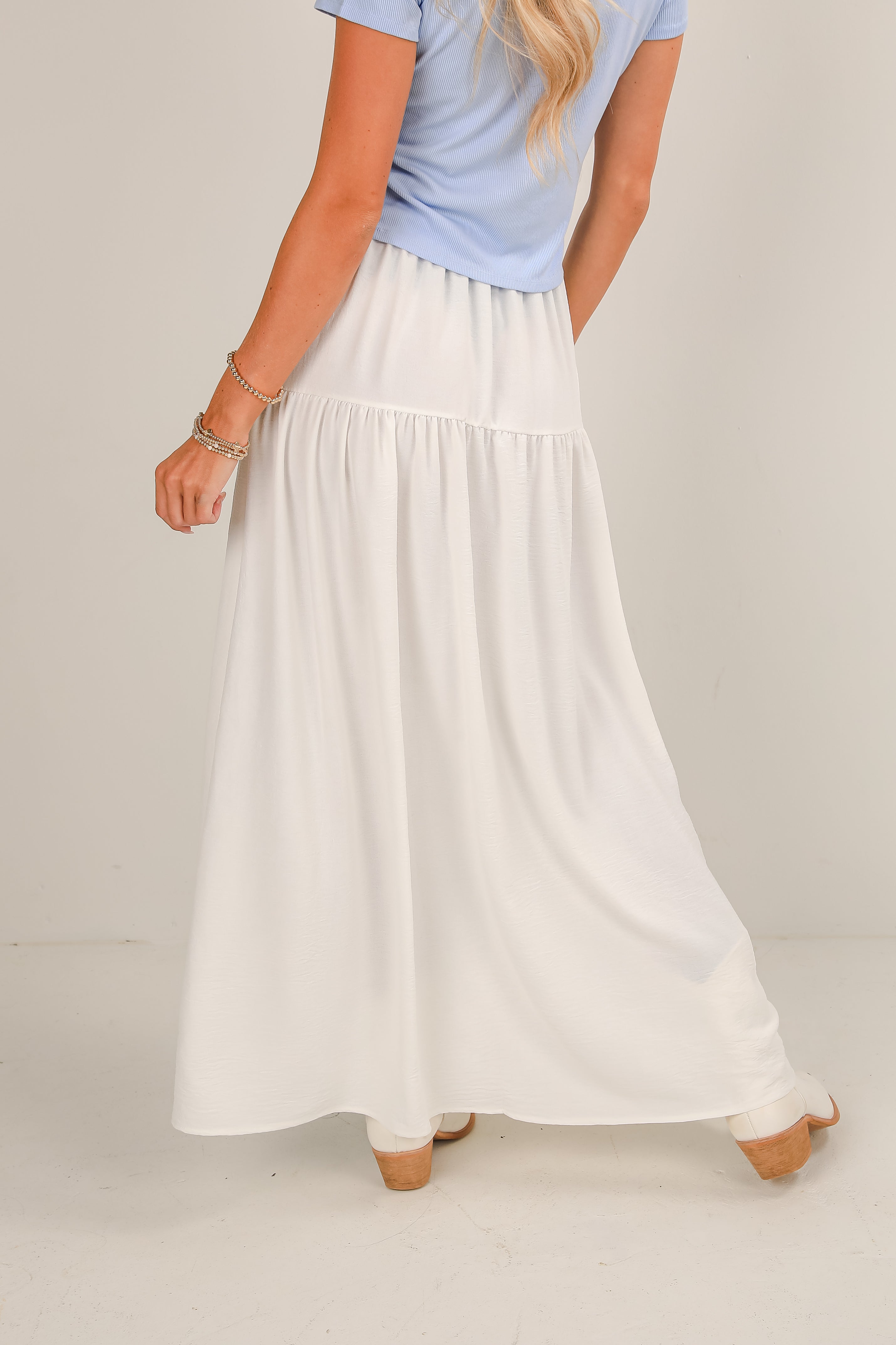 Person wearing a light blue shirt and white skirt on a plain background