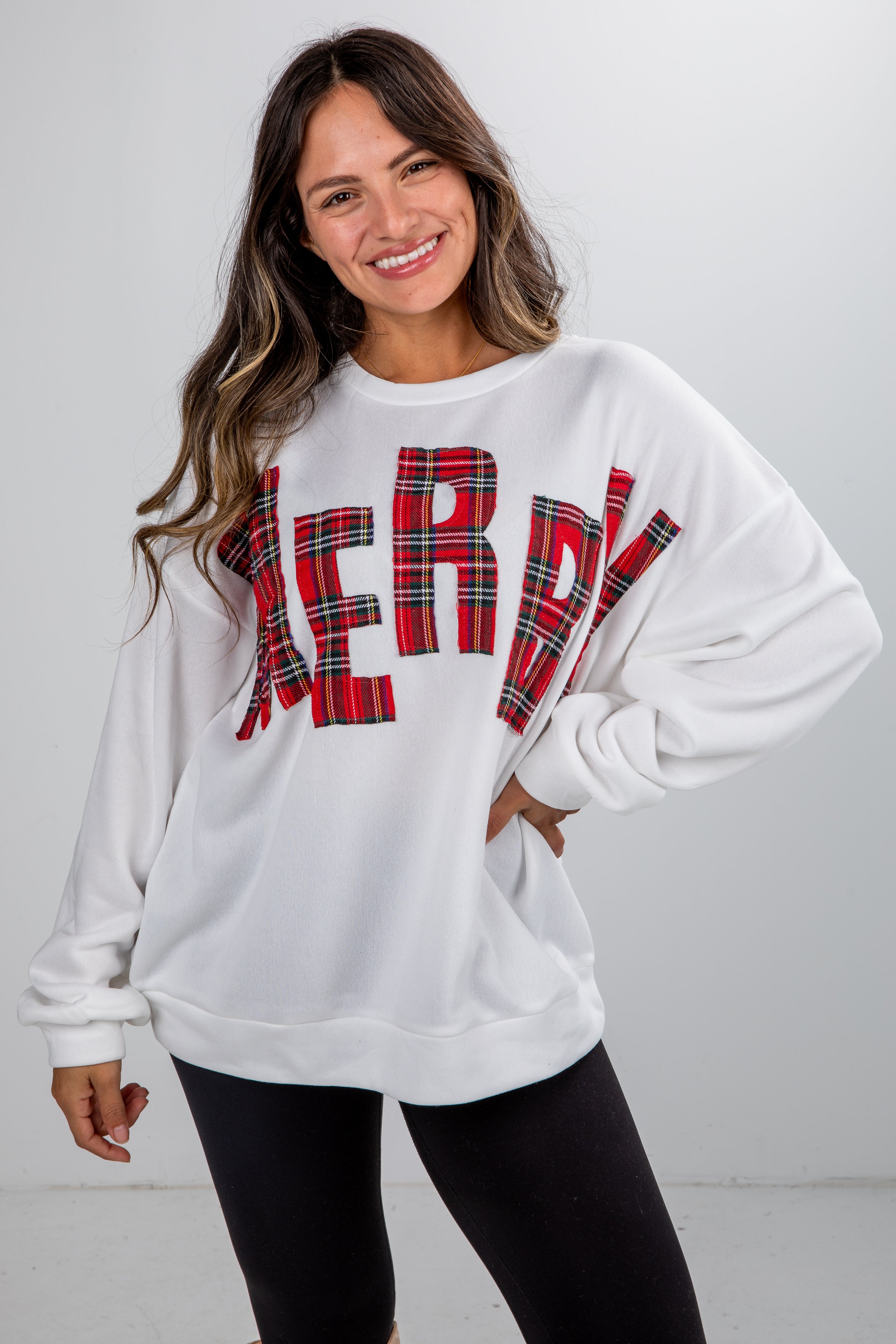 Woman wearing a white sweatshirt with red plaid letters spelling &