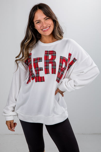 Woman wearing a white sweatshirt with red plaid letters spelling &
