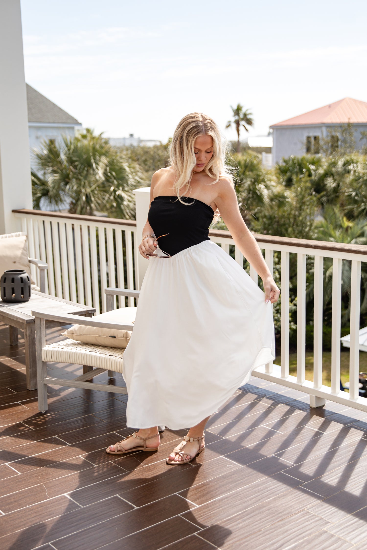 Woman in a black top and white skirt standing on a balcony with greenery in the background