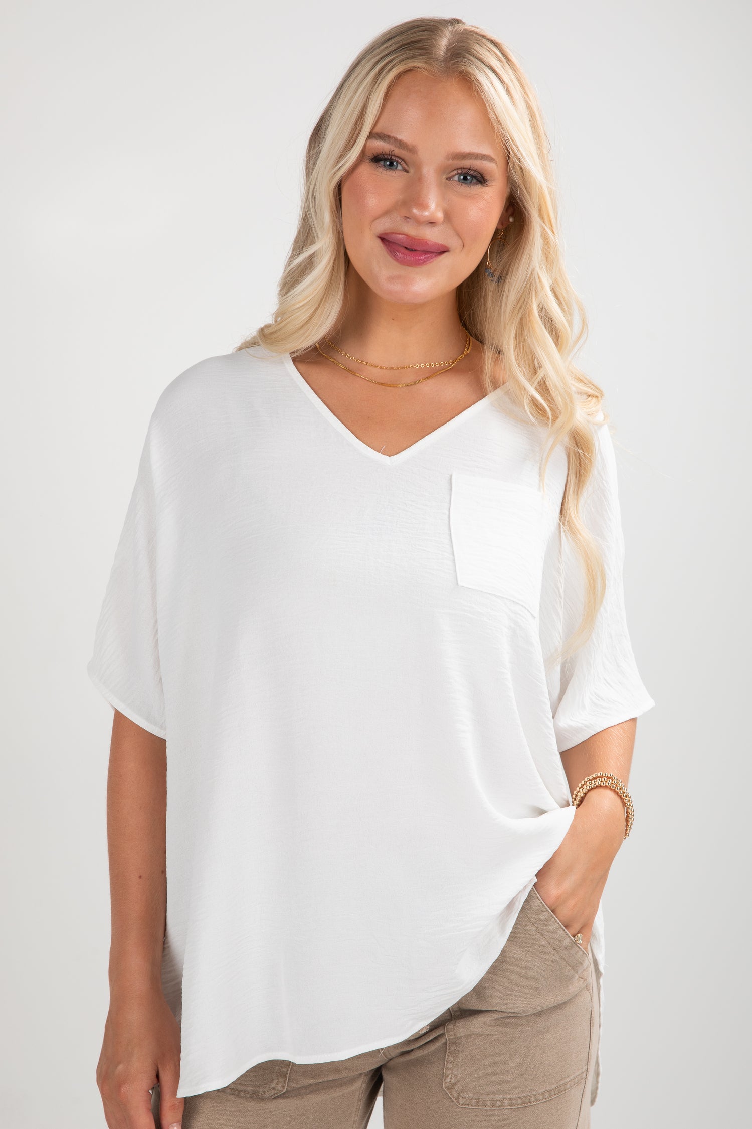 Woman wearing a white oversized t-shirt and beige pants on a plain background