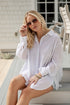 Woman in a white shirt sitting outdoors, wearing sunglasses.