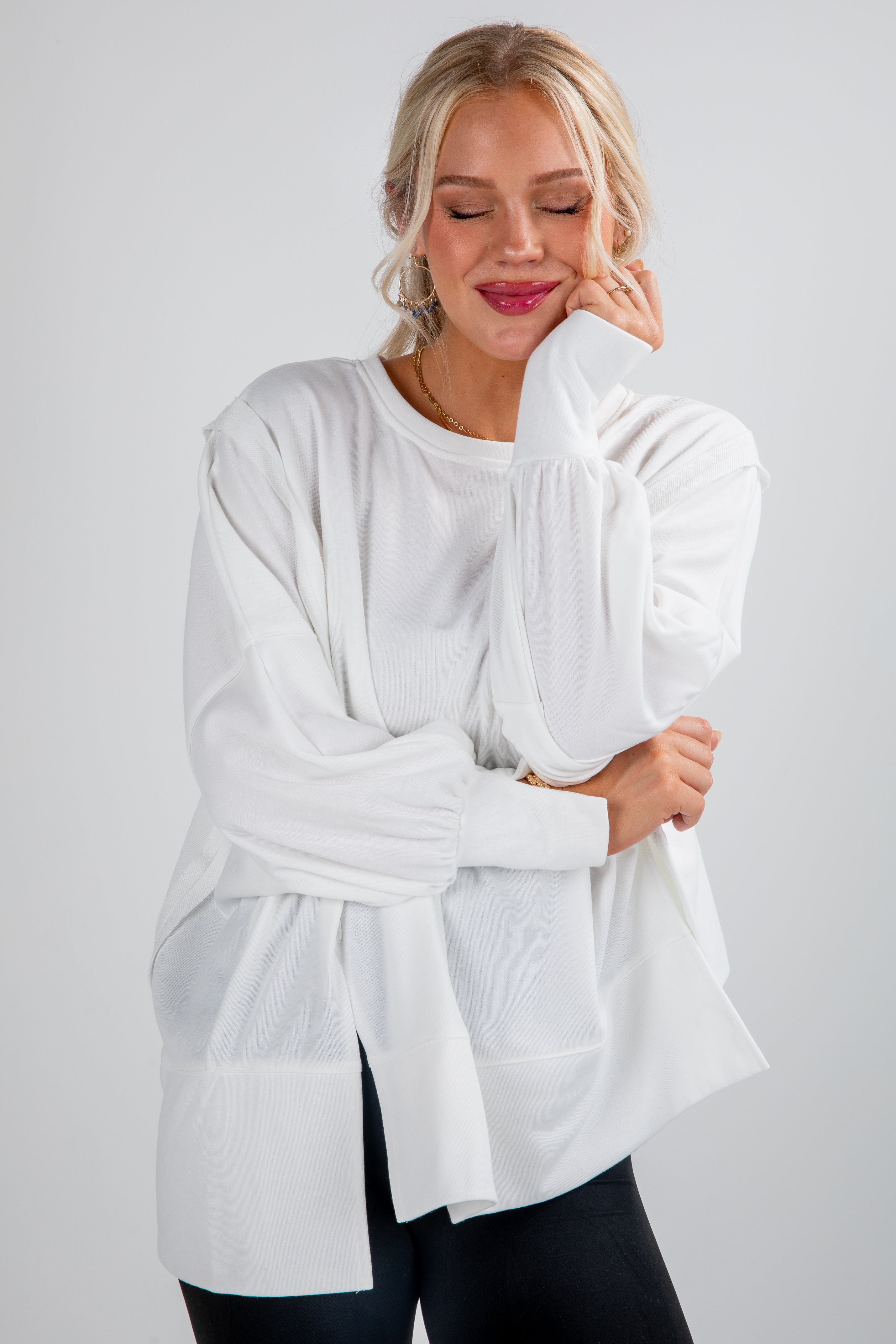 Woman wearing a white long-sleeve top against a plain background