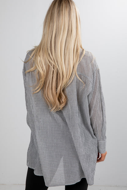 Person wearing a gray checkered shirt with long blonde hair, standing against a white background