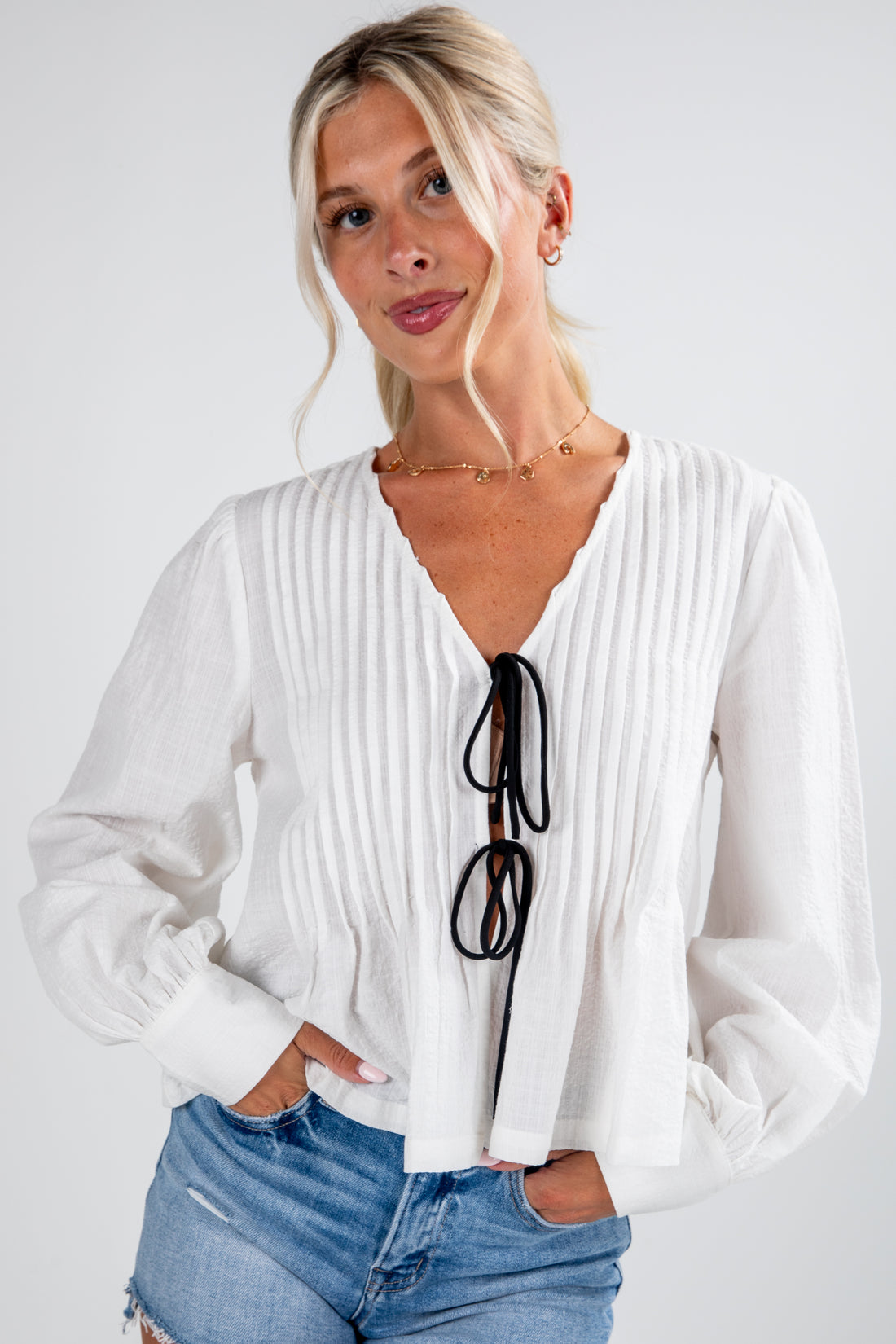 Woman wearing a white blouse with a deep neckline and blue jeans on a plain background