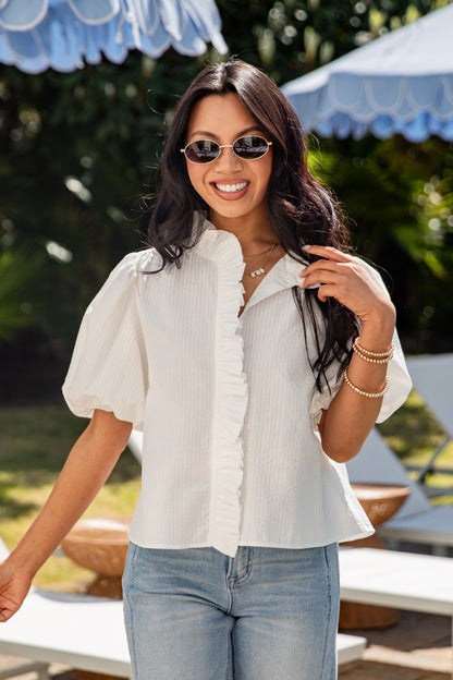 Woman wearing a white blouse and sunglasses outdoors with blurred background