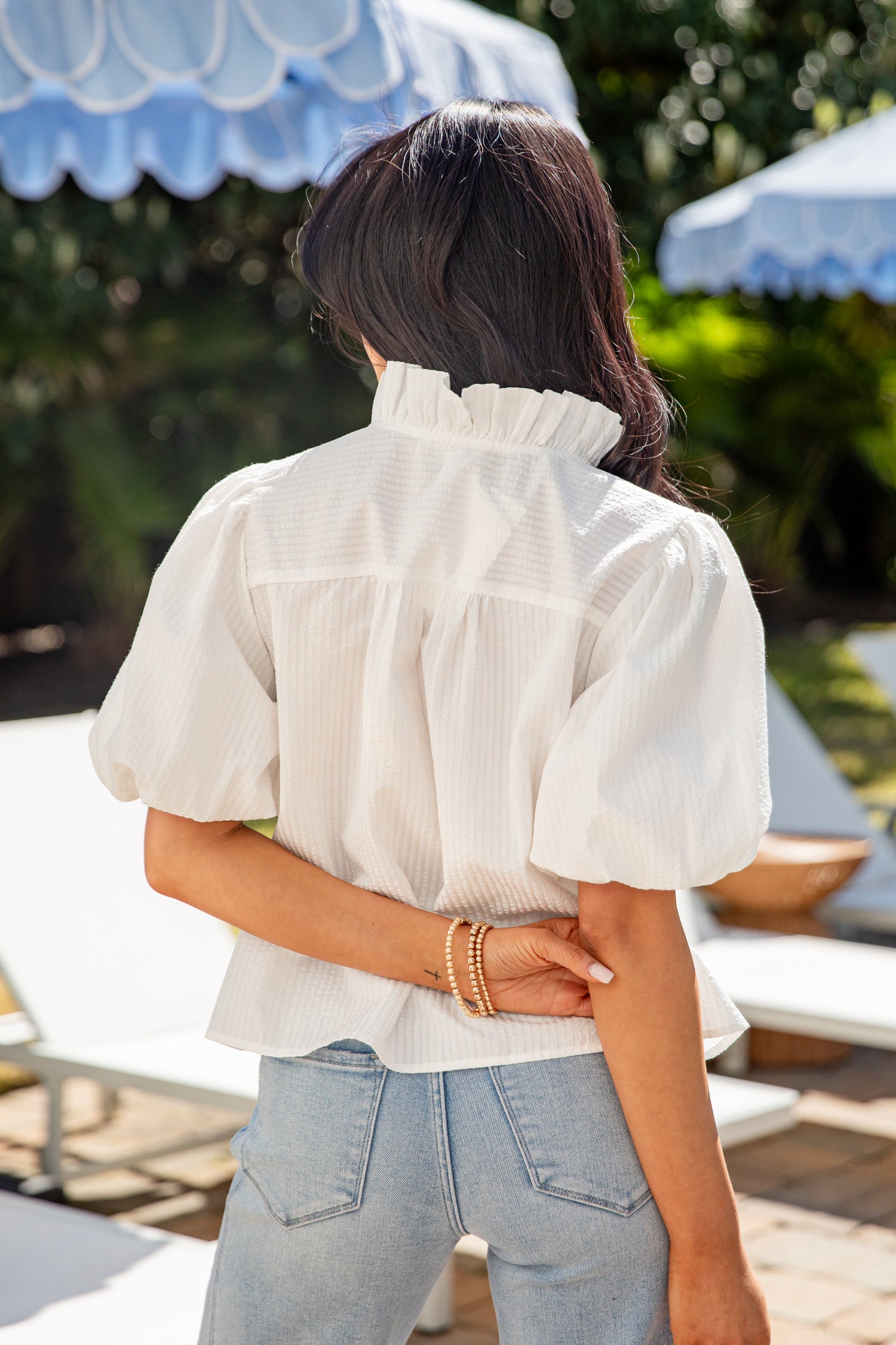 Person wearing a white blouse and light blue jeans with a blurred outdoor background