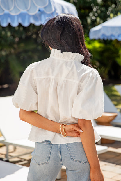 Person wearing a white blouse and light blue jeans with a blurred outdoor background