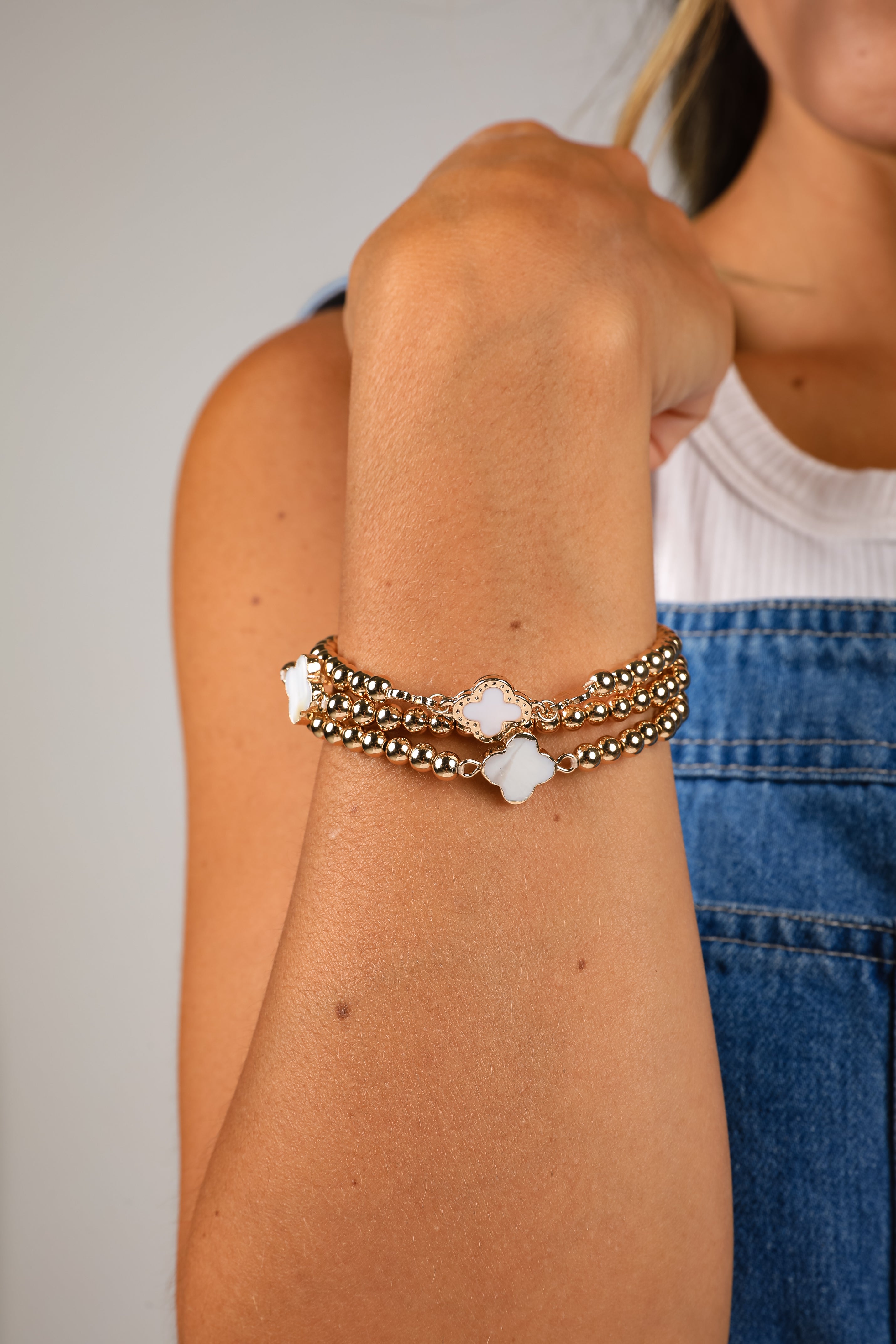 Person wearing a stack of bracelets on their wrist with a neutral background