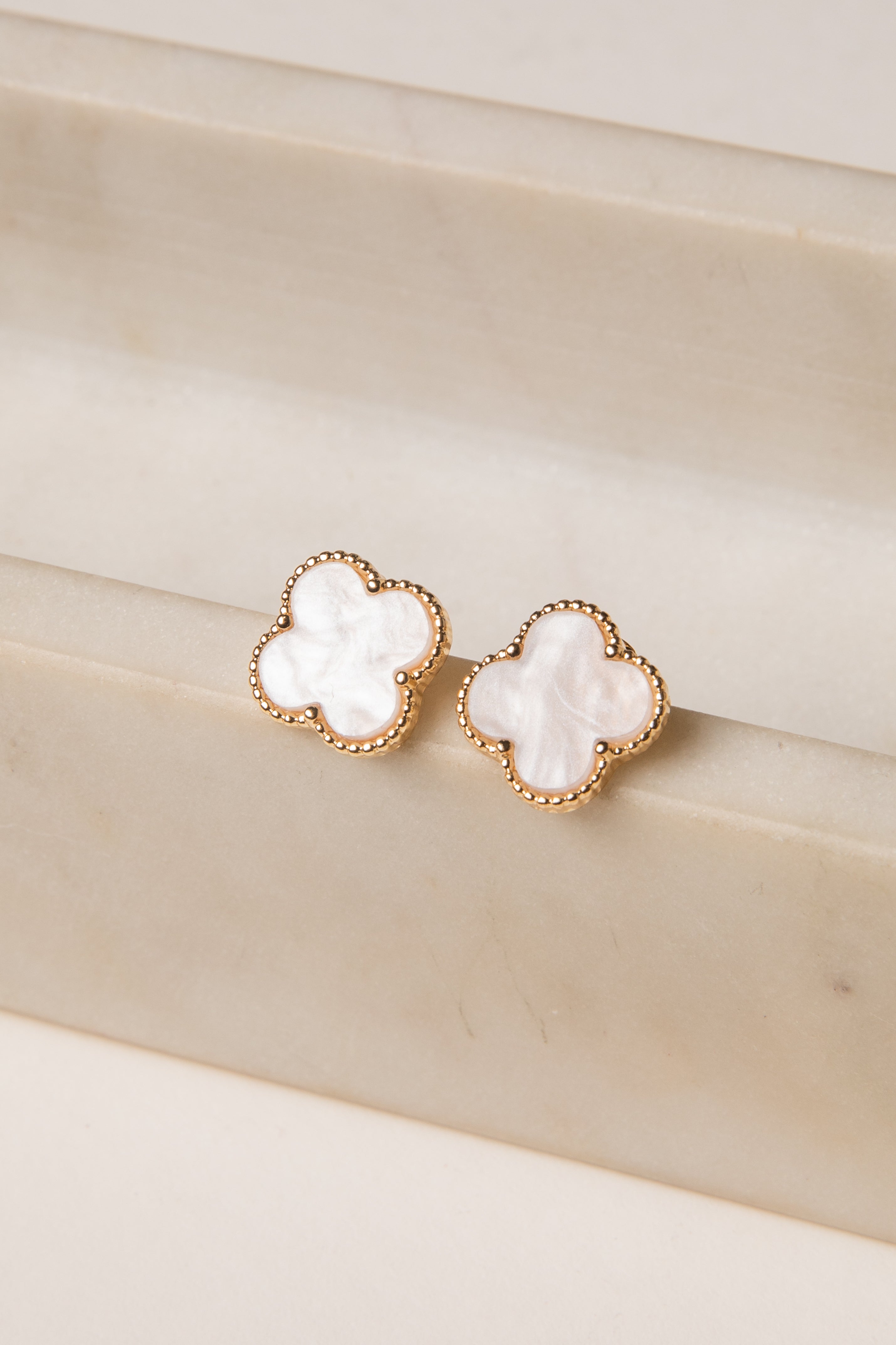 Pair of gold earrings with white stones on a beige surface