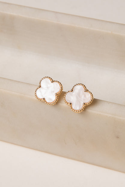 Pair of gold earrings with white stones on a beige surface
