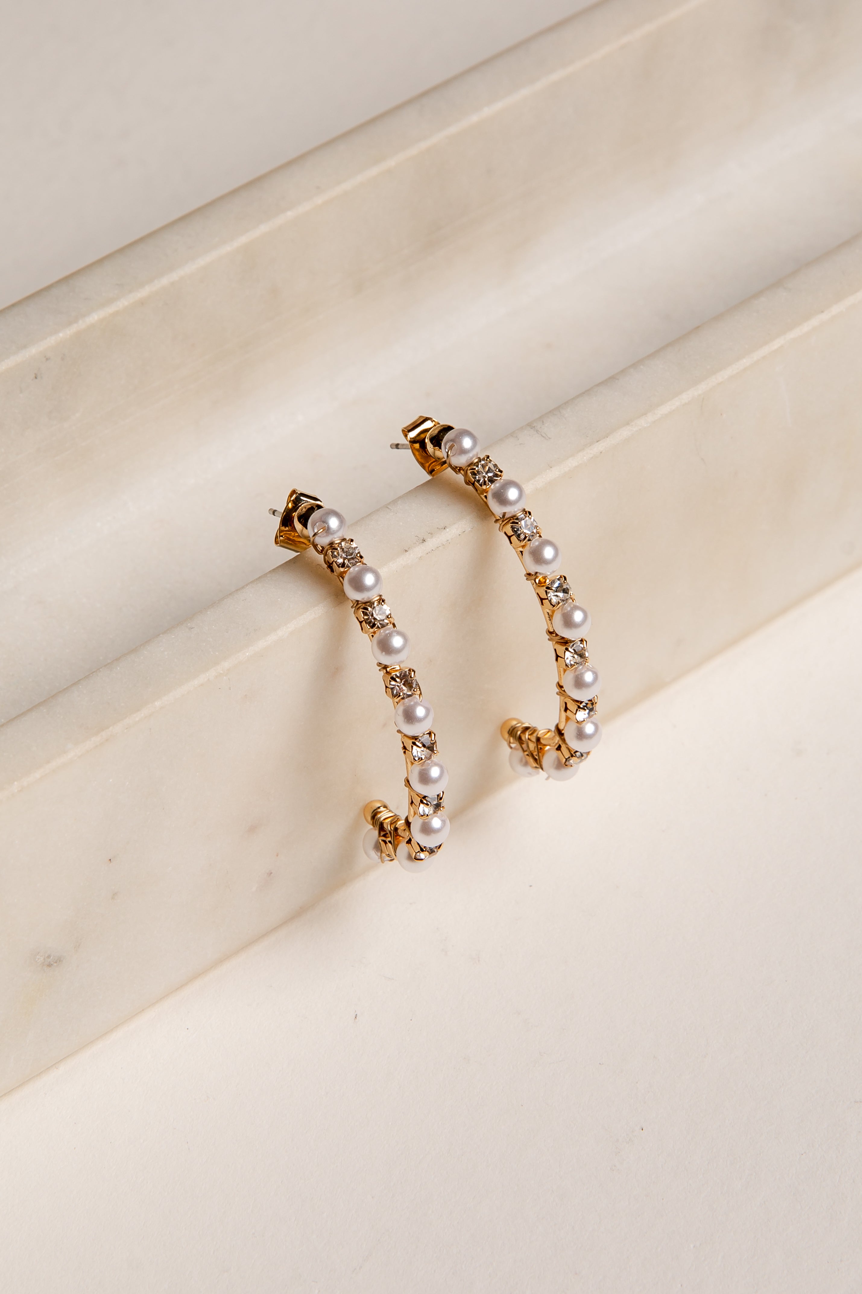 Gold hoop earrings with pearls on a beige surface