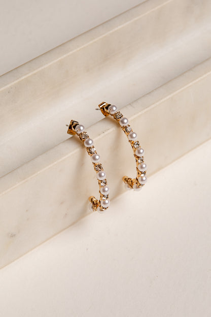 Gold hoop earrings with pearls on a beige surface