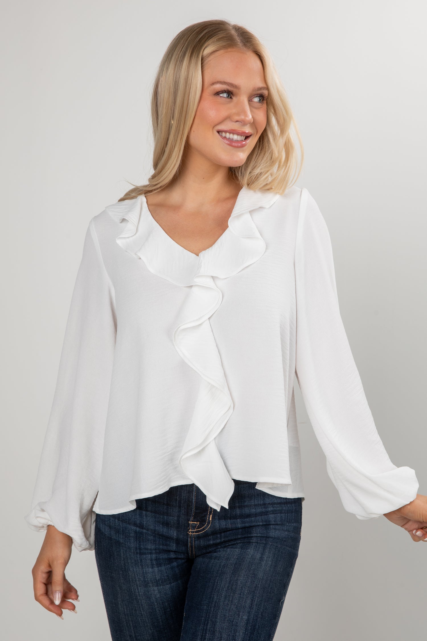 Woman wearing a white blouse with a ruffled design and blue jeans on a plain background
