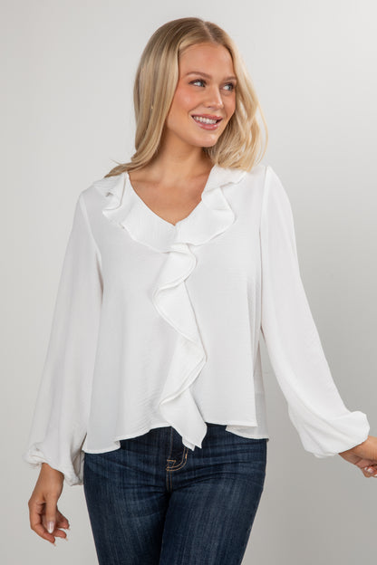 Woman wearing a white blouse with a ruffled design and blue jeans on a plain background
