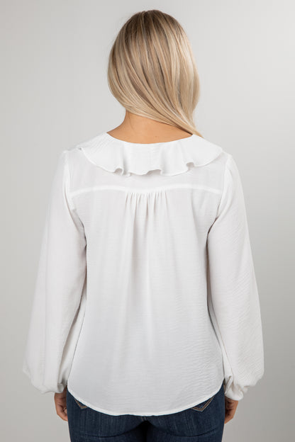 Person wearing a white blouse with ruffled collar on a plain background