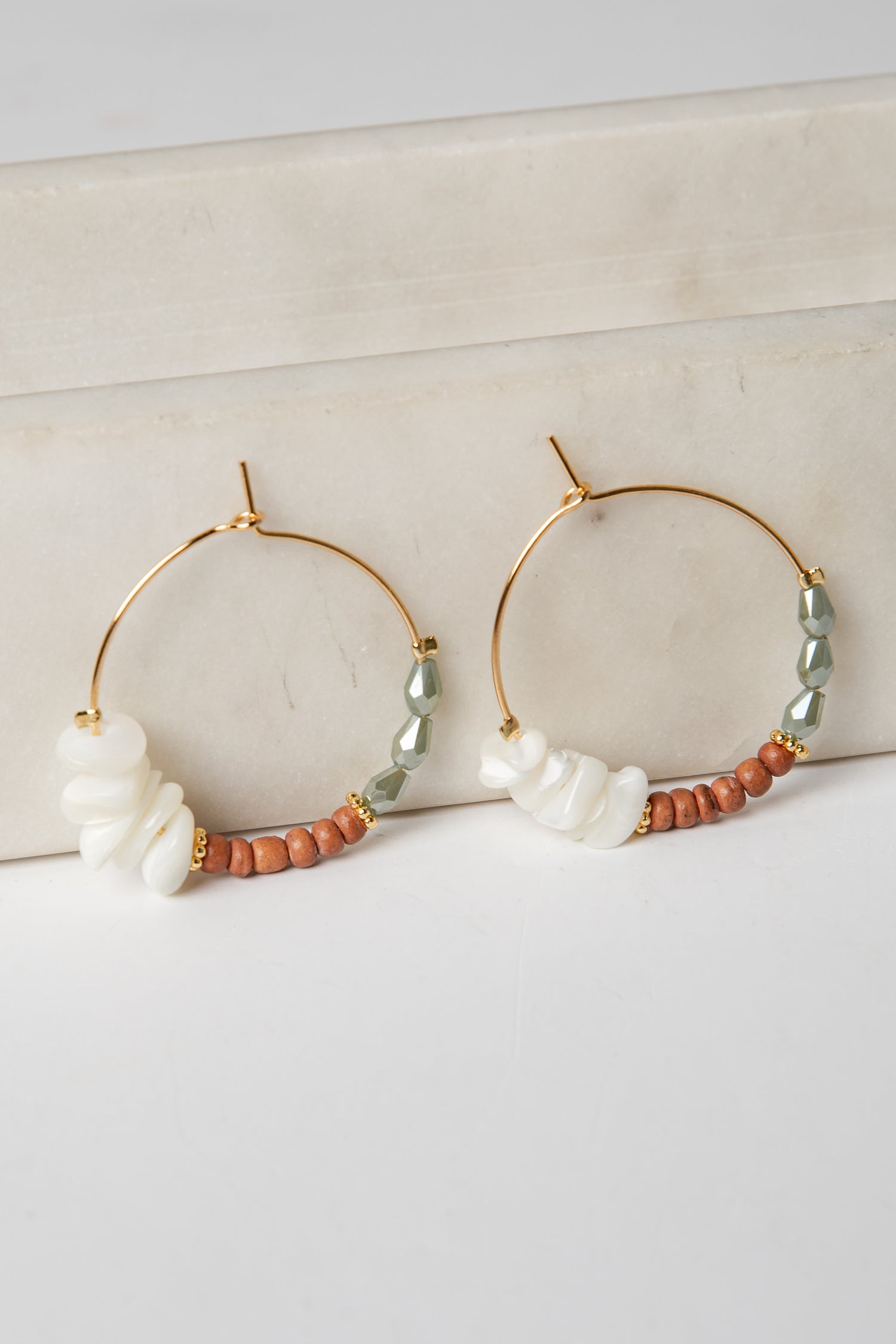 Gold hoop earrings with pearls and beads on a light background