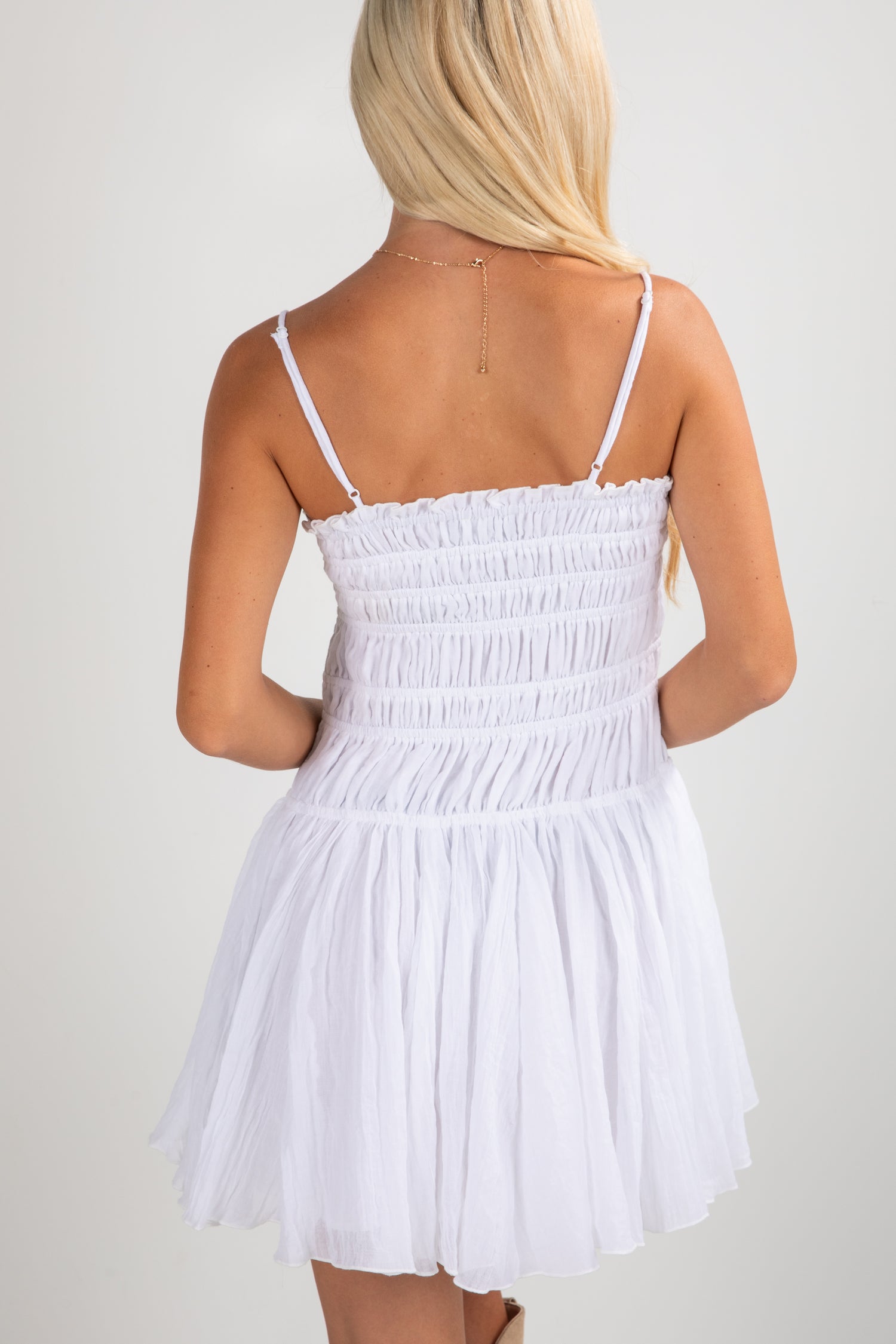 White dress with thin straps worn by a person on a plain background