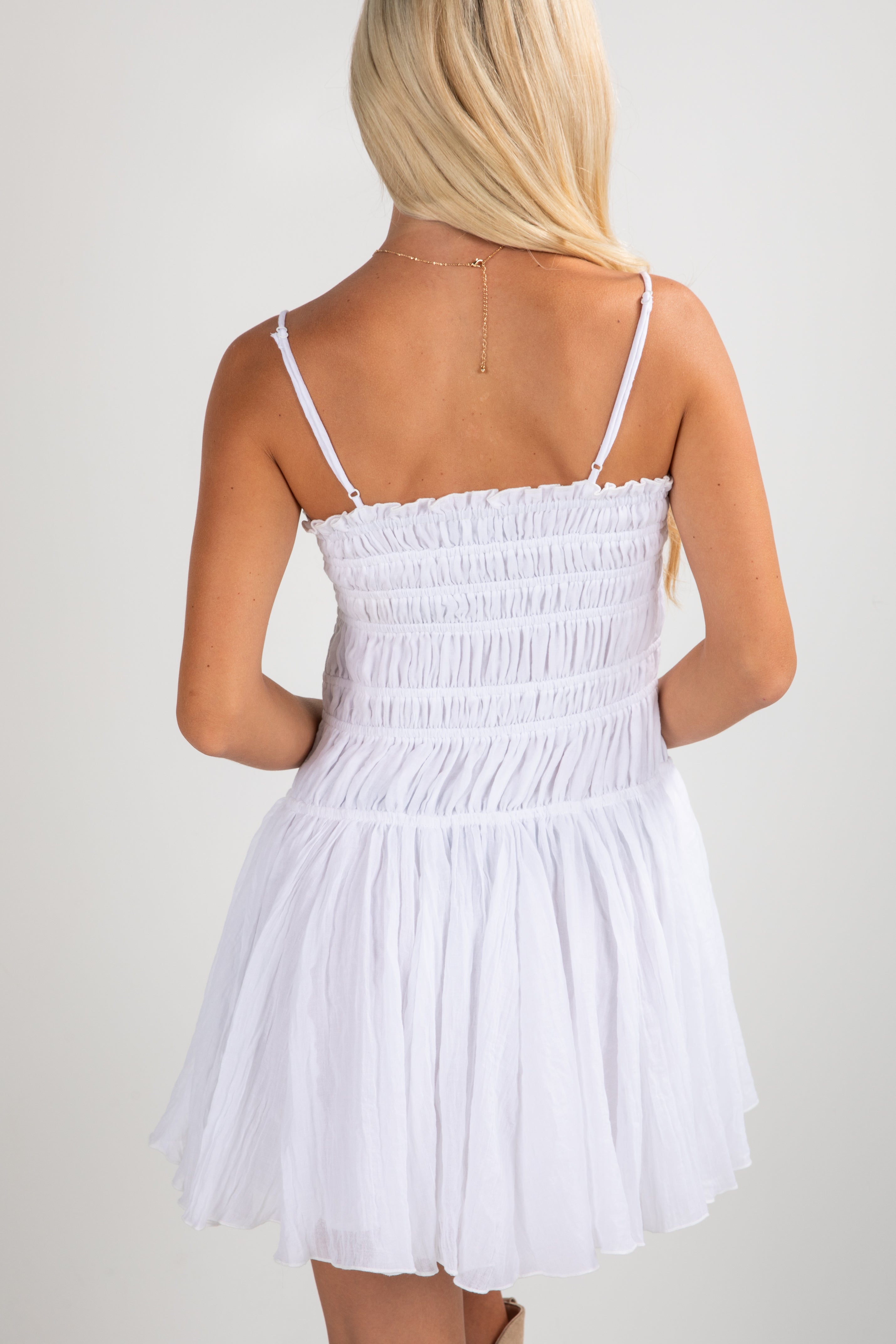 White dress with thin straps worn by a person on a plain background