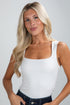 Woman wearing a white tank top against a plain background