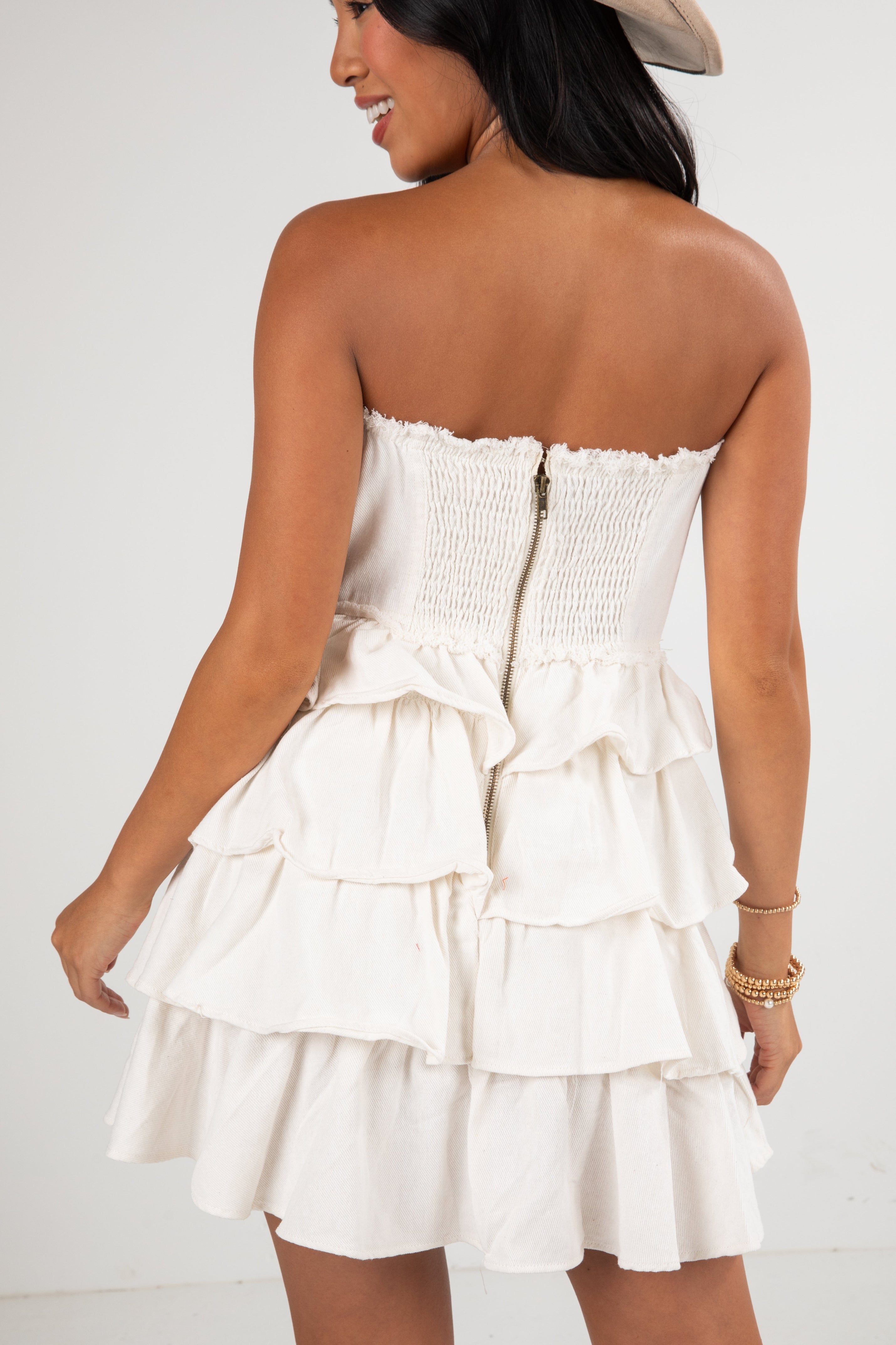 Woman wearing a white strapless dress with ruffled layers on a plain background