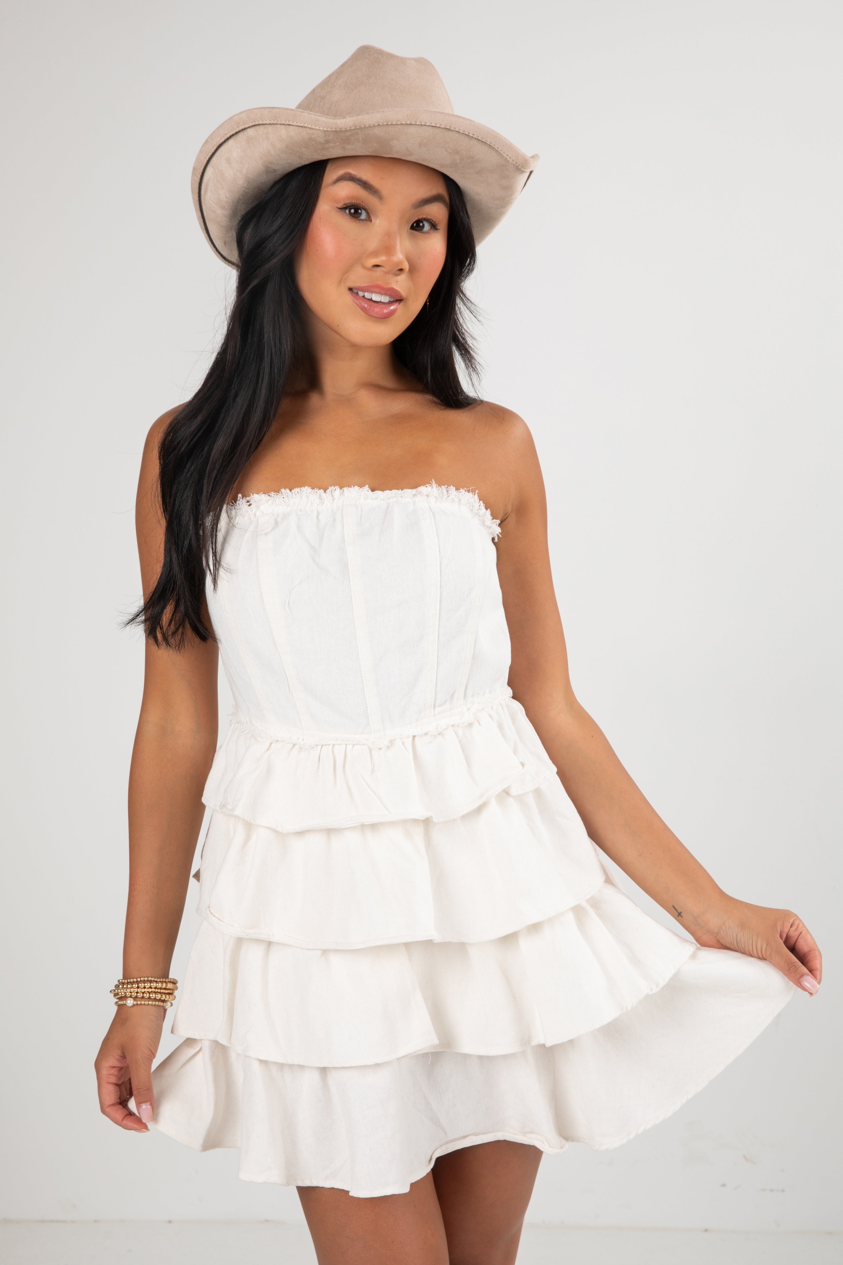 Woman wearing a white strapless dress and beige hat on a plain background