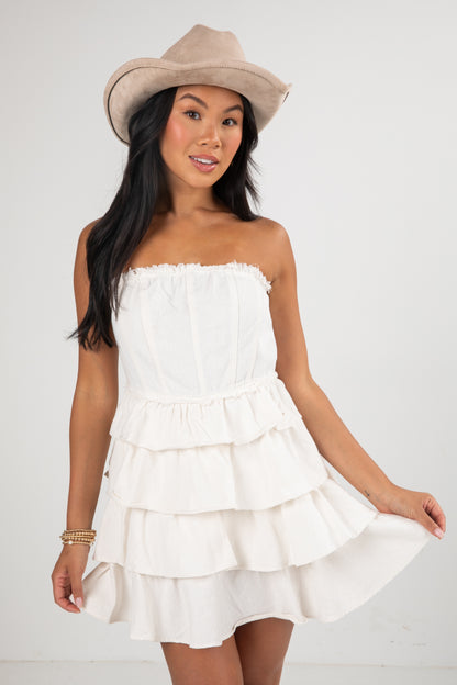 Woman wearing a white strapless dress and beige hat on a plain background