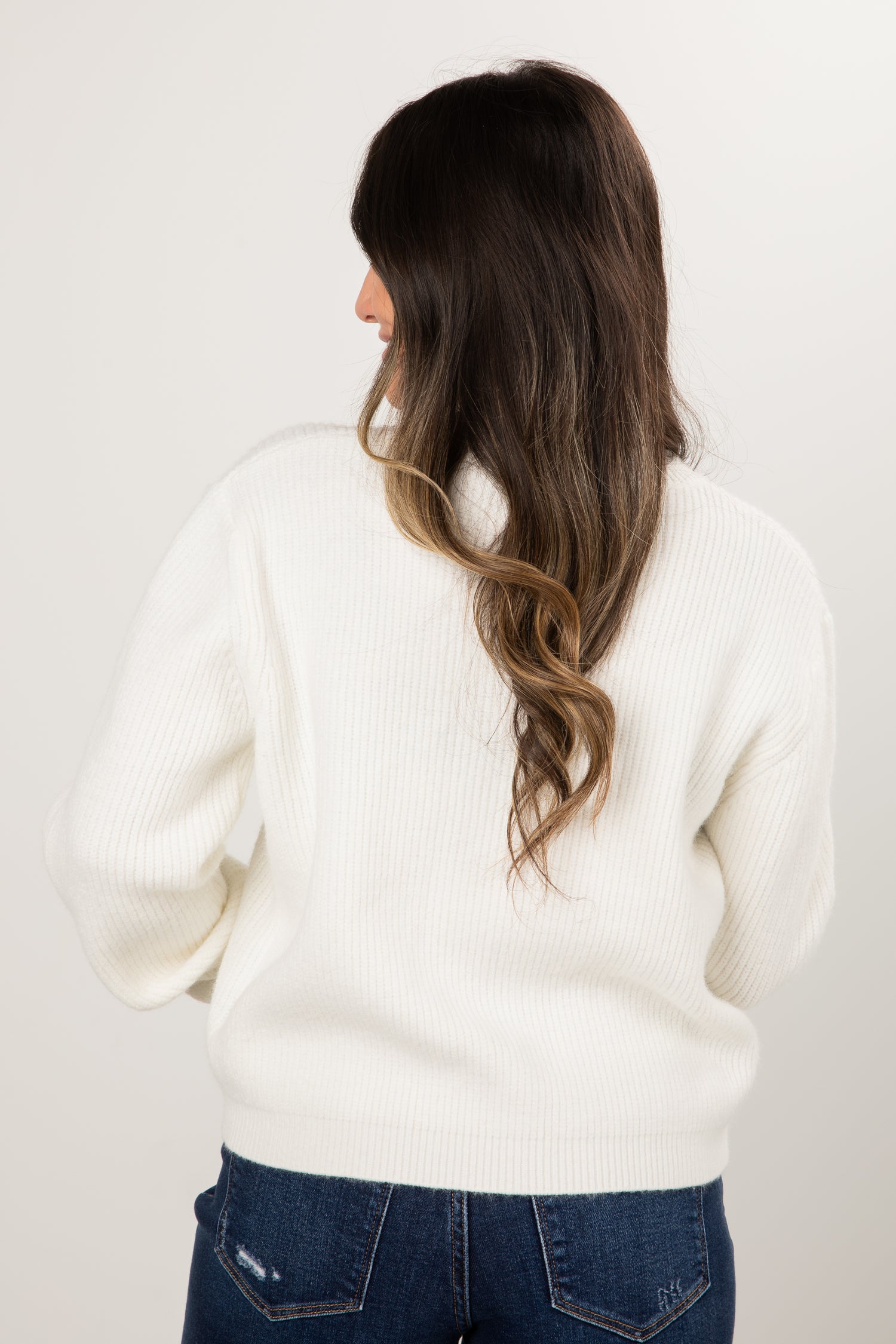 Woman wearing a white sweater and blue jeans against a plain background