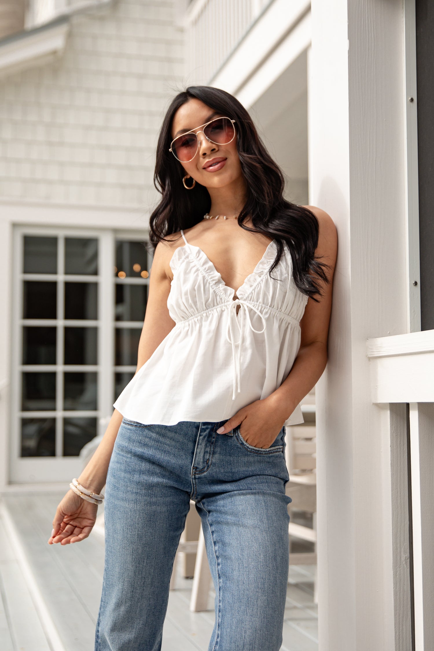 Woman wearing a white top and blue jeans, standing outdoors.
