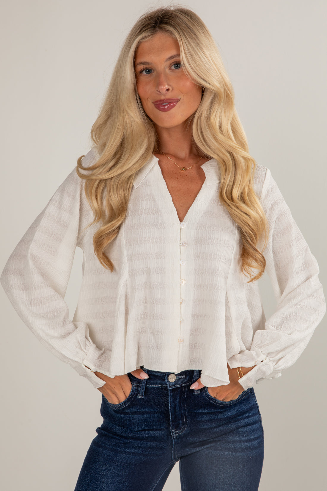 Woman wearing a white blouse and blue jeans against a plain background