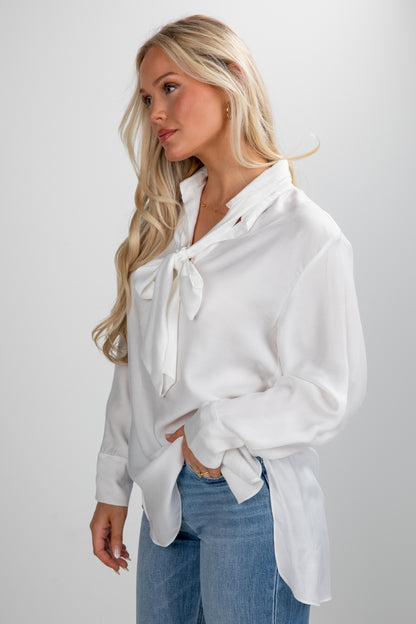 Woman wearing a white blouse with a bow tie and blue jeans on a plain background