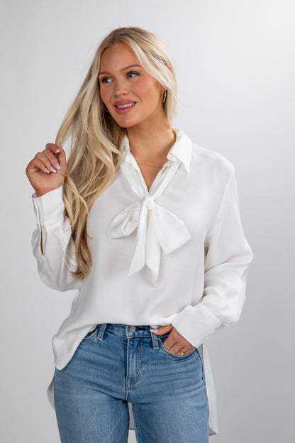 Woman wearing a white blouse with a bow tie and blue jeans on a plain background