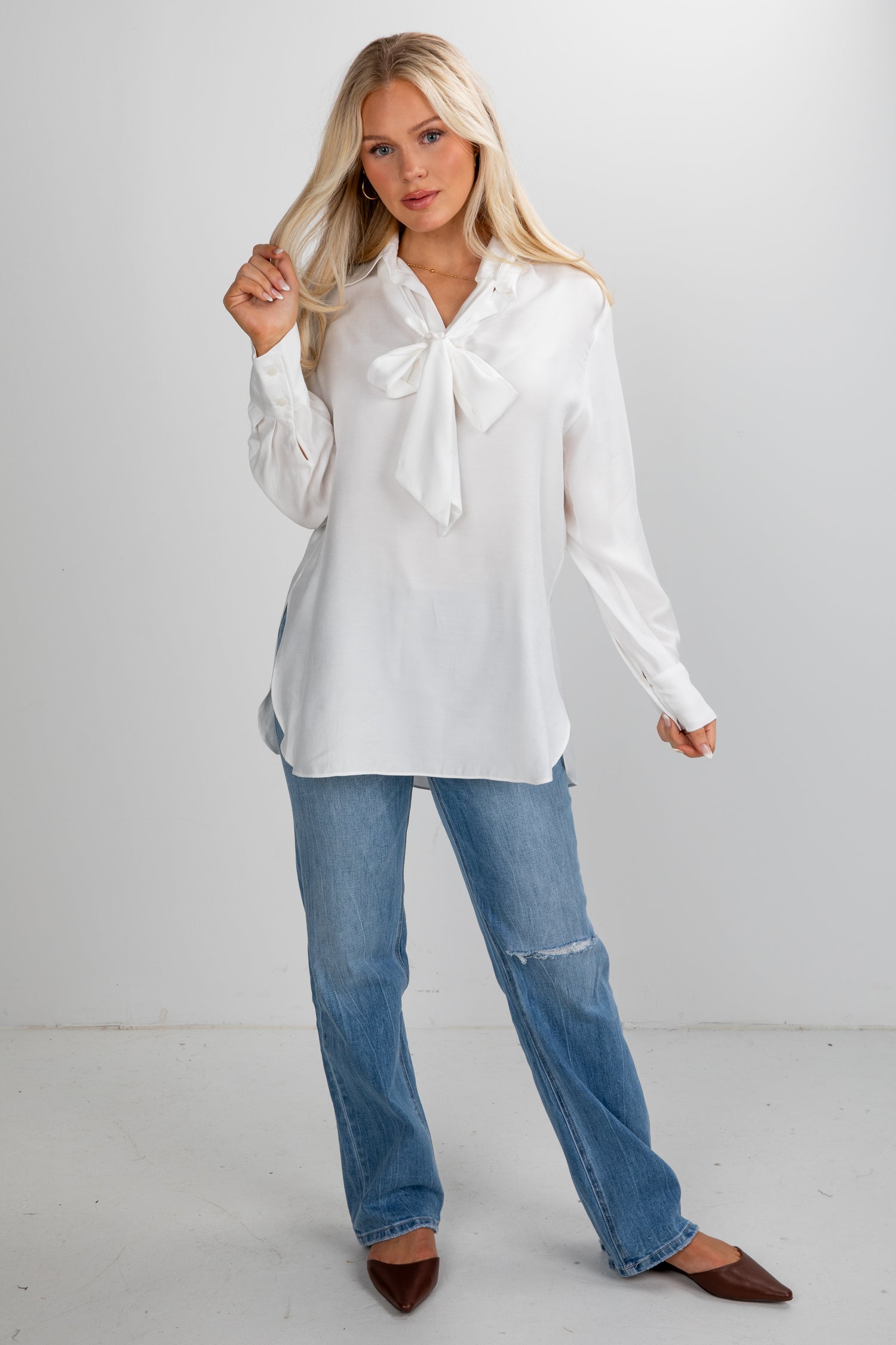 Woman wearing a white blouse with a bow tie and blue jeans on a white background