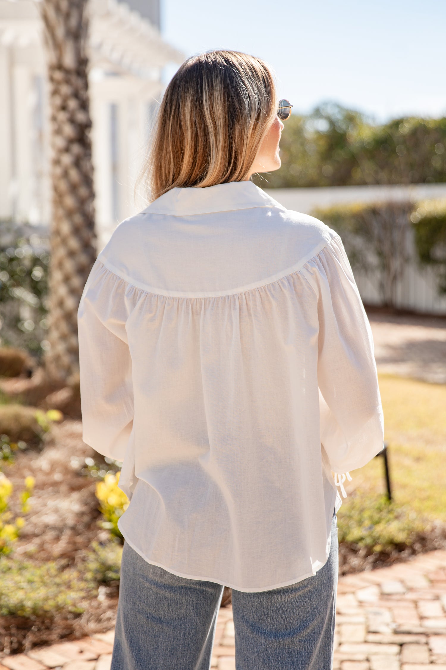 Woman wearing a white blouse outdoors with greenery in the background