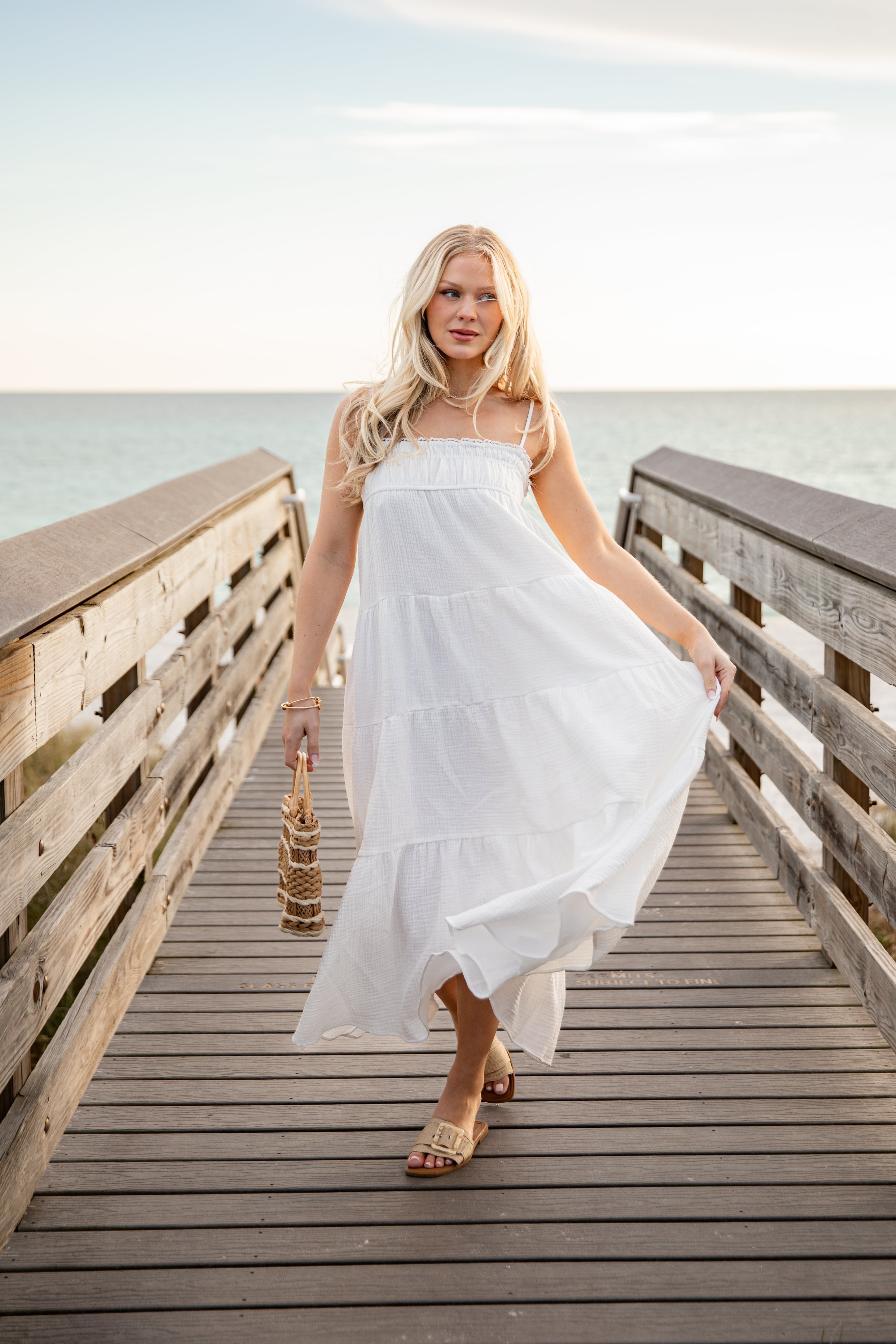 Woman in a white dress standing on a wooden pier by the water