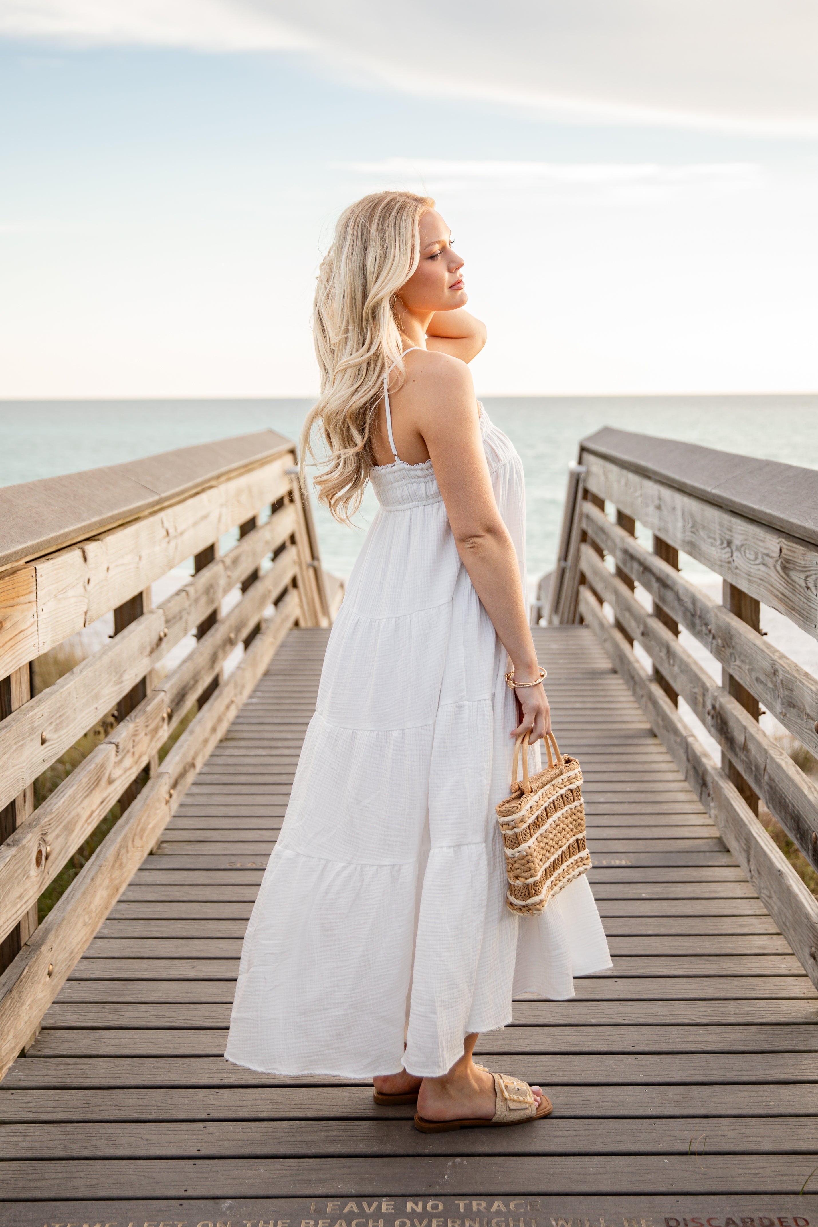 Woman in a white dress standing on a wooden pier by the sea