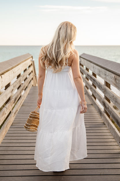 Woman in a white dress standing on a wooden pier by the water.
