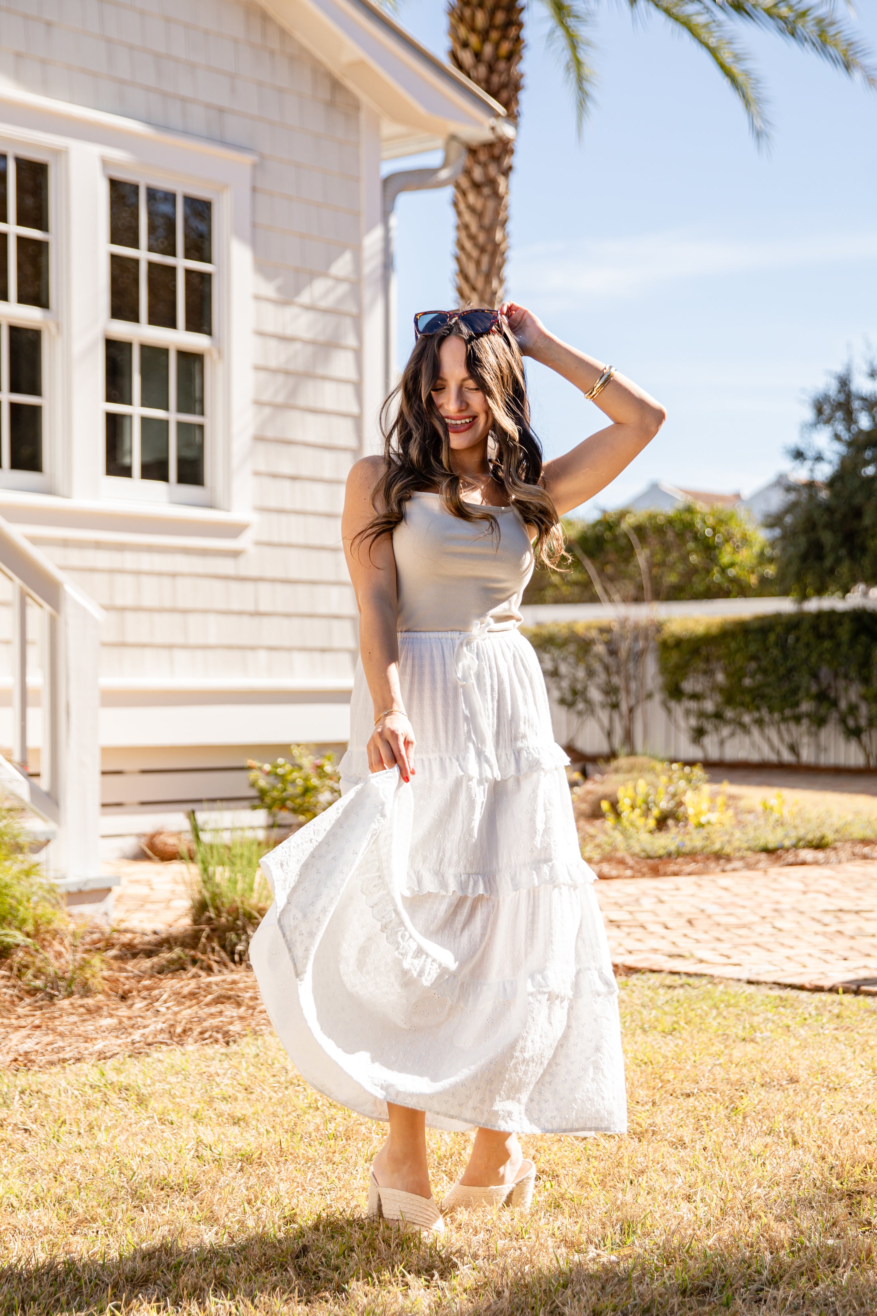 Woman in a white dress standing in front of a house with palm trees in the background