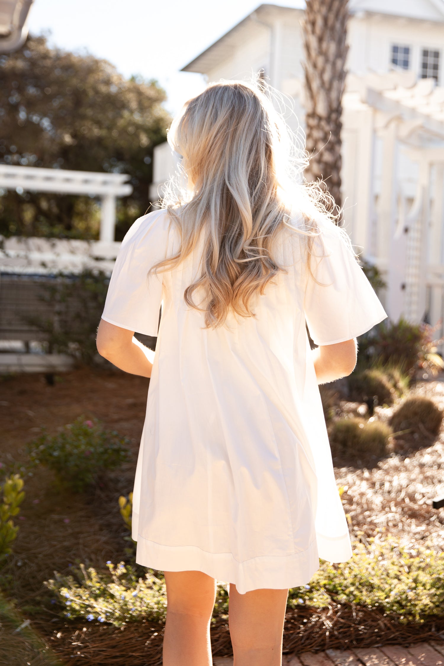 Person wearing a white dress with sheer sleeves in a garden setting