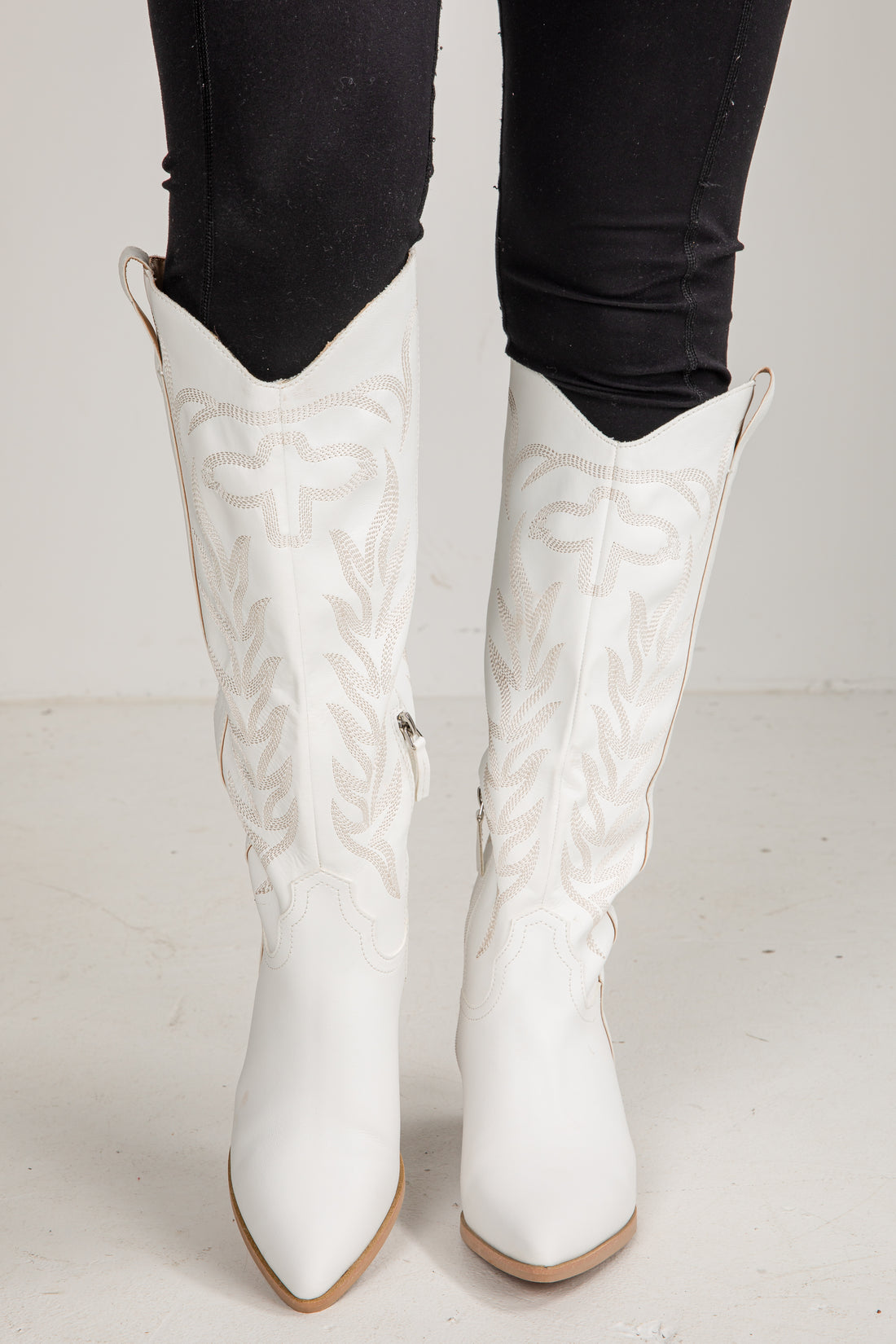White knee-high boots with black pants on a light background