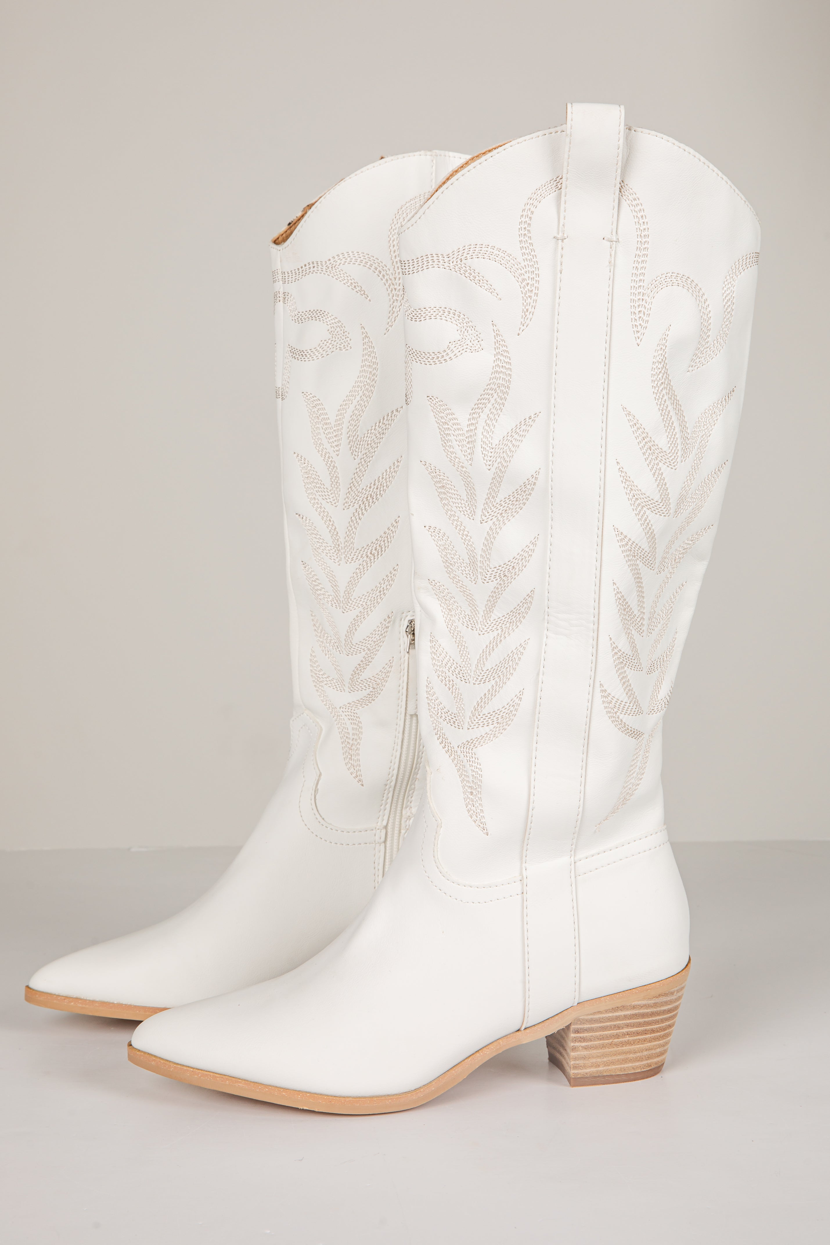 White cowboy boots with braided design on a light gray background